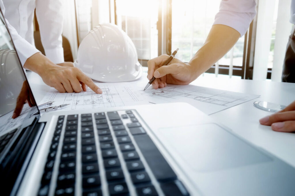 Architects reviewing plans beside a laptop and hard hat, as mobile apps change construction