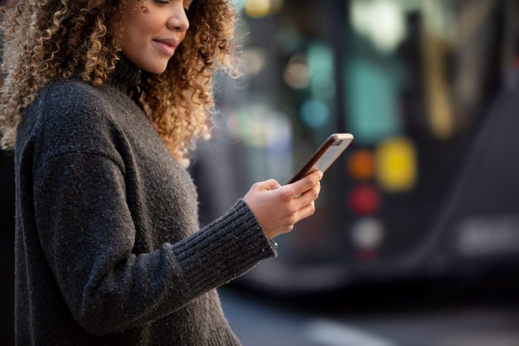 Woman using her phone at a bus stop, the everyday user a future-proof app must serve