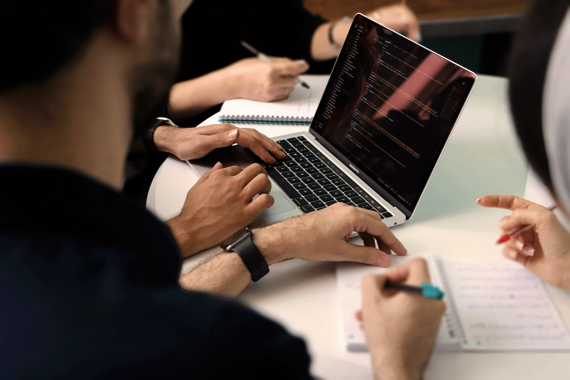 Software developers collaborating on code during a team meeting, laptop screen with code and notes