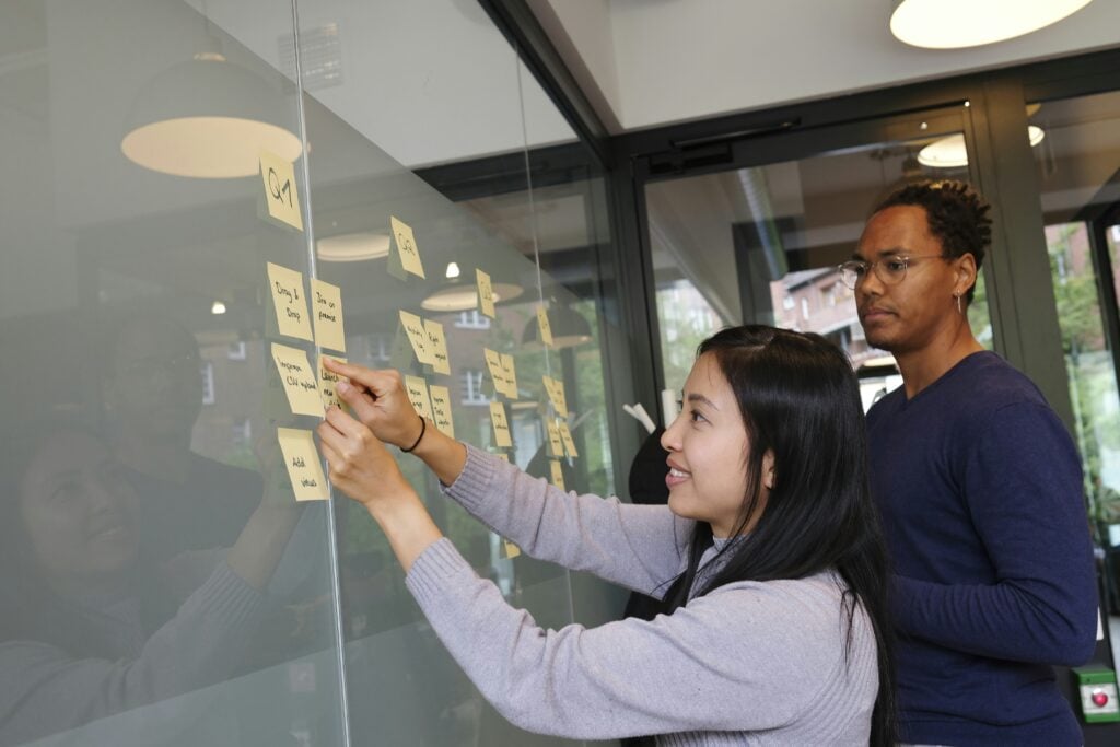 Two colleagues collaborating on an agile planning session using sticky notes on a glass wall