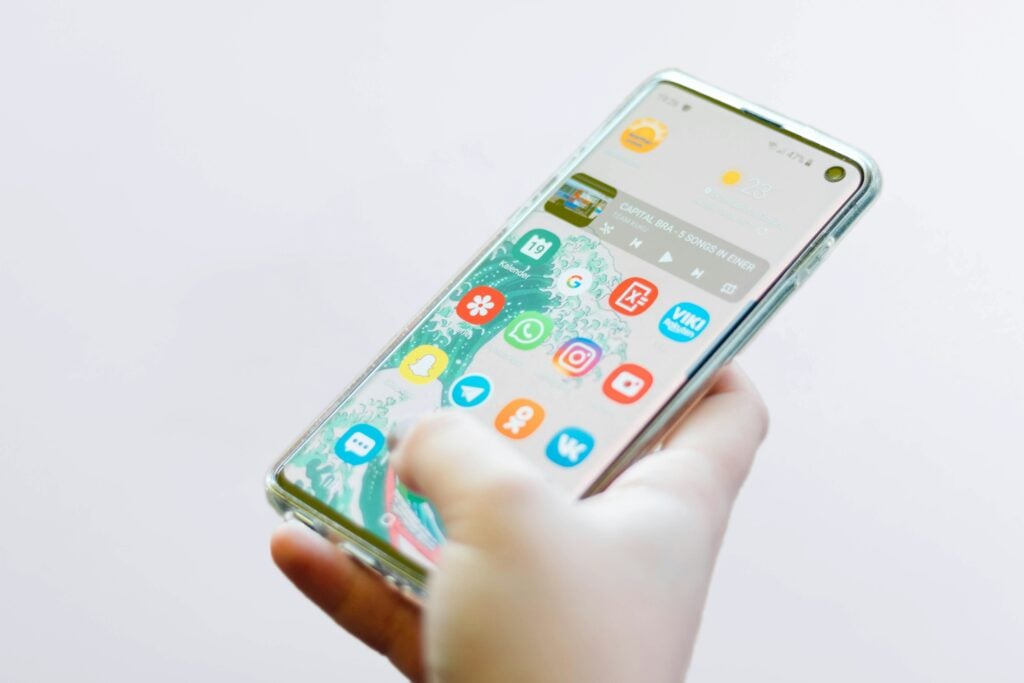Hand holding a smartphone full of app icons, illustrating the cost of building an app