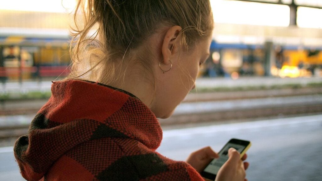 Woman using her phone on a train platform, the user tech investment should serve