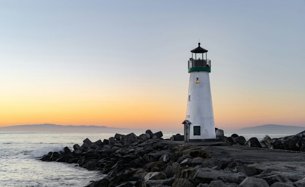 Lighthouse on a rocky shore at sunset, representing moving from pilot projects to proof